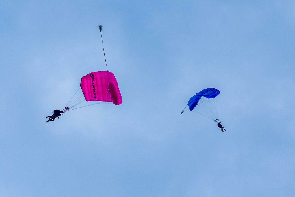 two skydivers under their blue and pink parachutes