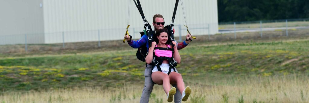 tandem skydivers landing, the instructor is male and the student is female in a pink tank top