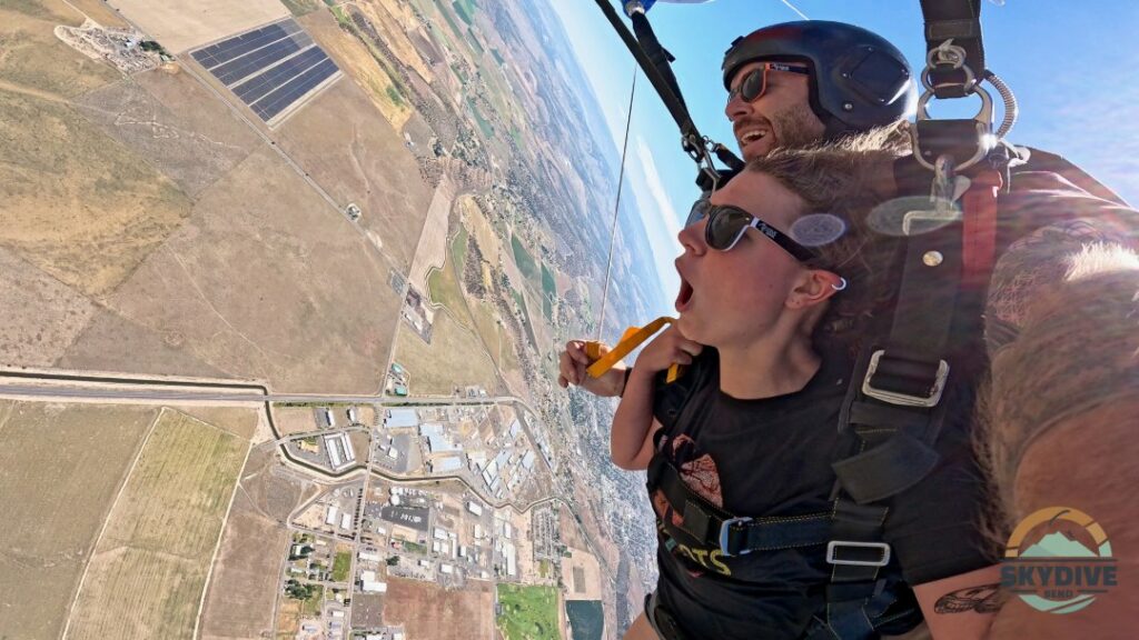 female tandem skydiver opens her mouth in awe while flying under the parachute, her instructor is smiling